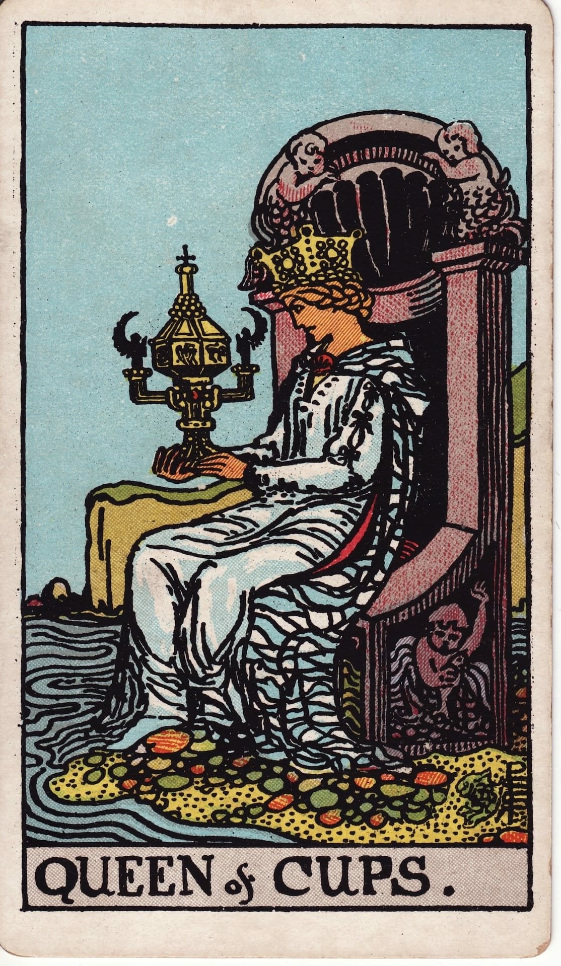 The Queen of Cups tarot card showing a woman sitting by the sea with a golden, lidded chalice.